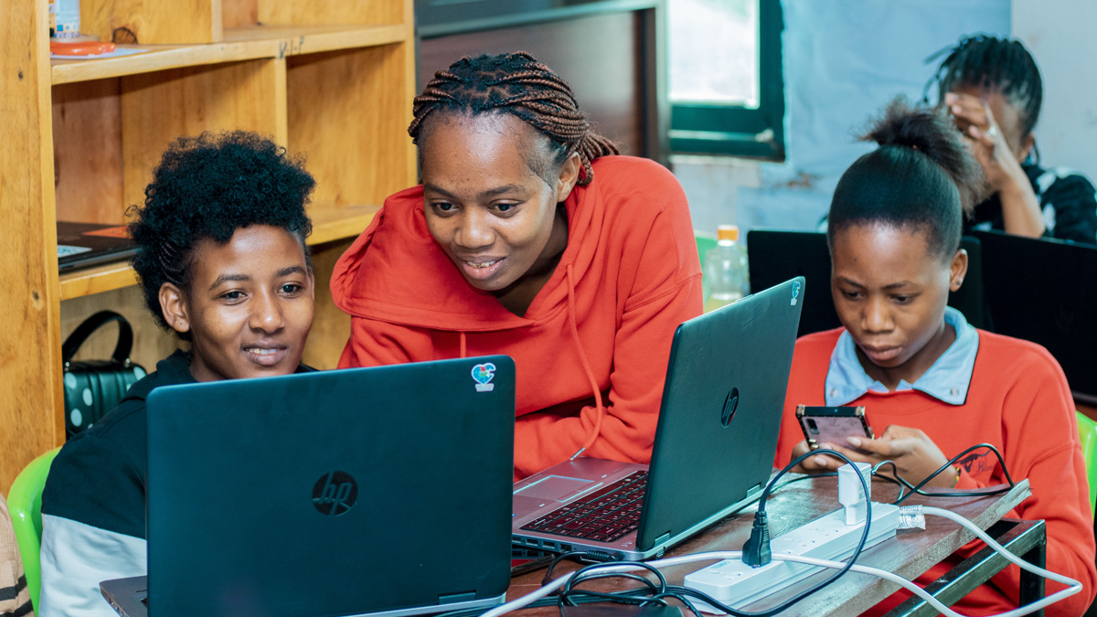 Three young people using laptops and a smartphone in a study area.