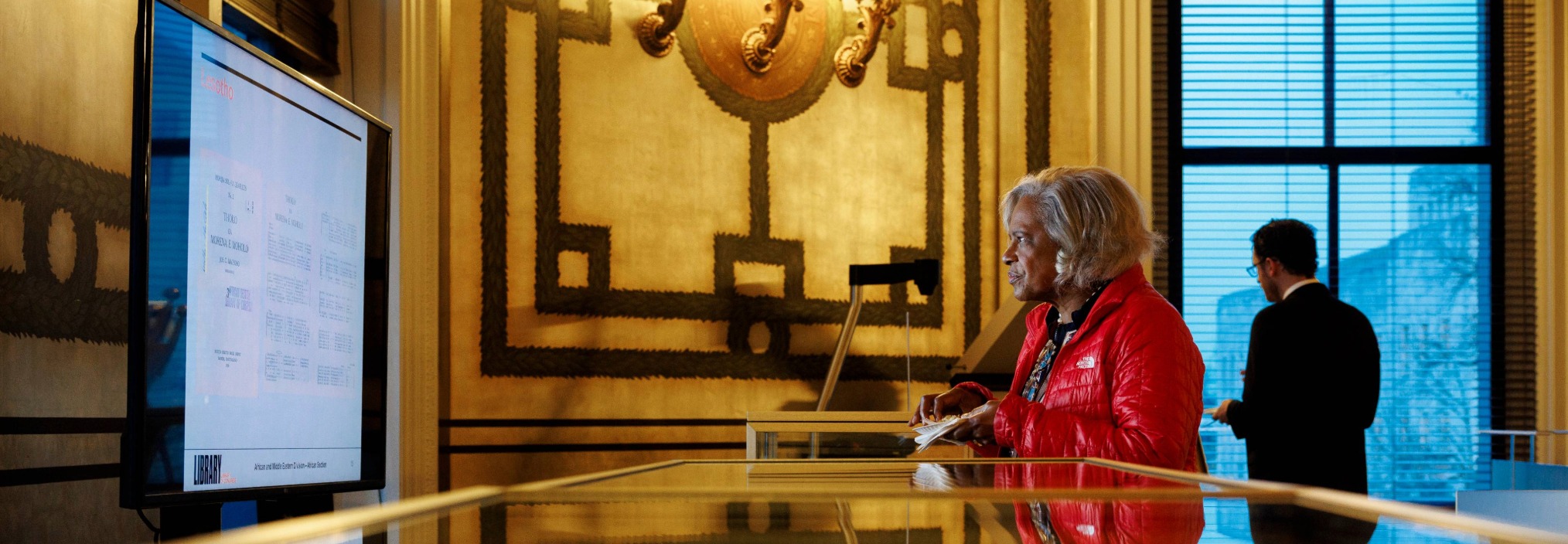 A woman in a red jacket looks at a large screen in a Reading Room at the Library of Congress.